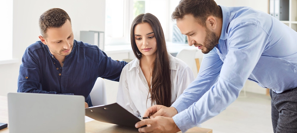 Couple of clients discuss a contract with a financial consultant or banker during a meeting in the office. Conversation with agent focuses on investment strategies and contract agreements.